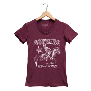 K&ouml;nnte beinhalten: Burgunderfarbenes T-Shirt mit einem wei&szlig;en Aufdruck einer Cowgirl, die ein Pferd reitet. Der Aufdruck enth&auml;lt den Text "COWGIRL" und "The WILD WEST".