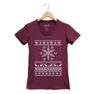 May include: A maroon t-shirt with a white snowflake and reindeer pattern. The shirt has a crew neck and short sleeves.