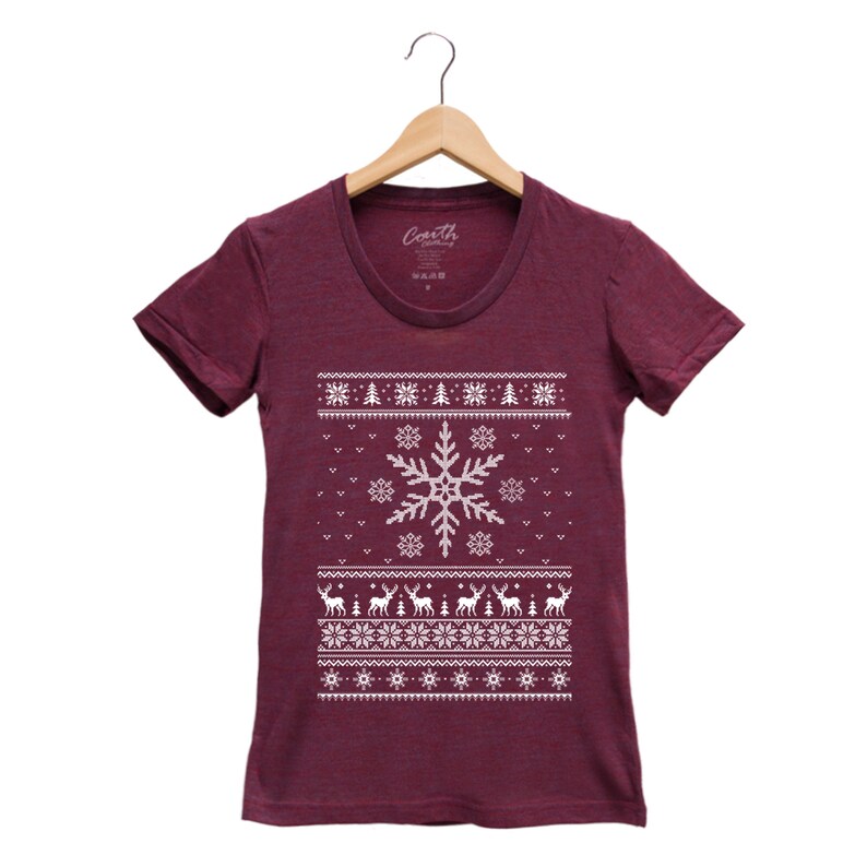 May include: A maroon t-shirt with a white snowflake and reindeer pattern. The shirt has a crew neck and short sleeves.