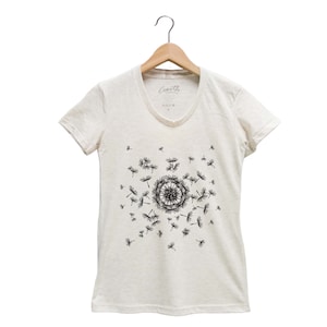 May include: A white v-neck t-shirt with a black dandelion design. The dandelion is in the center of the shirt and has seeds blowing off of it.