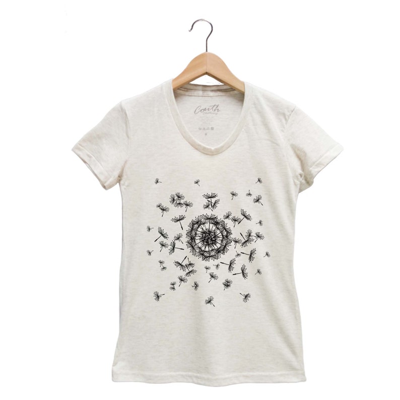 May include: A white v-neck t-shirt with a black dandelion design. The dandelion is in the center of the shirt and has seeds blowing off of it.