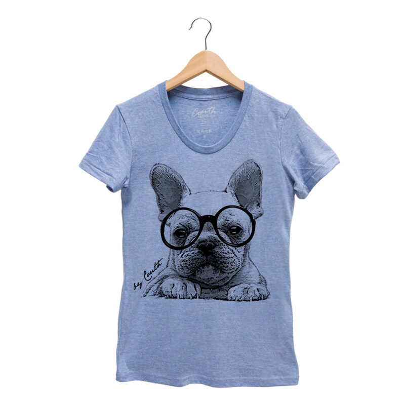 K&ouml;nnte beinhalten: Hellblaues T-Shirt mit einer schwarz-wei&szlig;en Illustration eines franz&ouml;sischen Bulldoggen, der eine runde Brille tr&auml;gt. Der Text "Dog Count" ist in Kursivschrift unten links auf dem T-Shirt geschrieben.