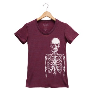 Puede incluir: Una camiseta de color granate con un gr&aacute;fico de esqueleto blanco. El esqueleto est&aacute; de frente con los brazos a los lados. La camiseta tiene un cuello redondo.