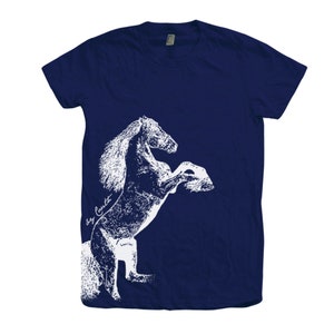 Op de afbeelding: Een marineblauw t-shirt met een wit silhouet van een paard dat op zijn achterpoten staat. Het paard is wit omlijnd en heeft een textuur.