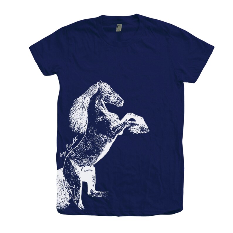 Op de afbeelding: Een marineblauw t-shirt met een wit silhouet van een paard dat op zijn achterpoten staat. Het paard is wit omlijnd en heeft een textuur.