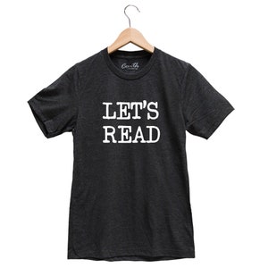 May include: A dark heather grey t-shirt with the text "LET'S READ" printed in white on the front.