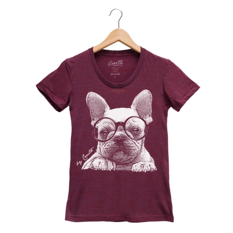K&ouml;nnte beinhalten: Burgunderfarbenes T-Shirt mit einer wei&szlig;en Grafik eines franz&ouml;sischen Bulldoggen, der eine runde Brille tr&auml;gt. Der Text "by Coyutt" ist unter dem Bild gedruckt.