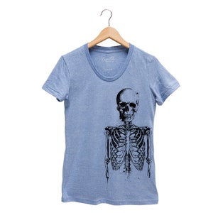 Puede incluir: Una camiseta azul claro con un estampado gr&aacute;fico en blanco y negro de un esqueleto. El esqueleto est&aacute; de pie con los brazos a los lados. El cr&aacute;neo est&aacute; mirando hacia adelante con una expresi&oacute;n neutral.