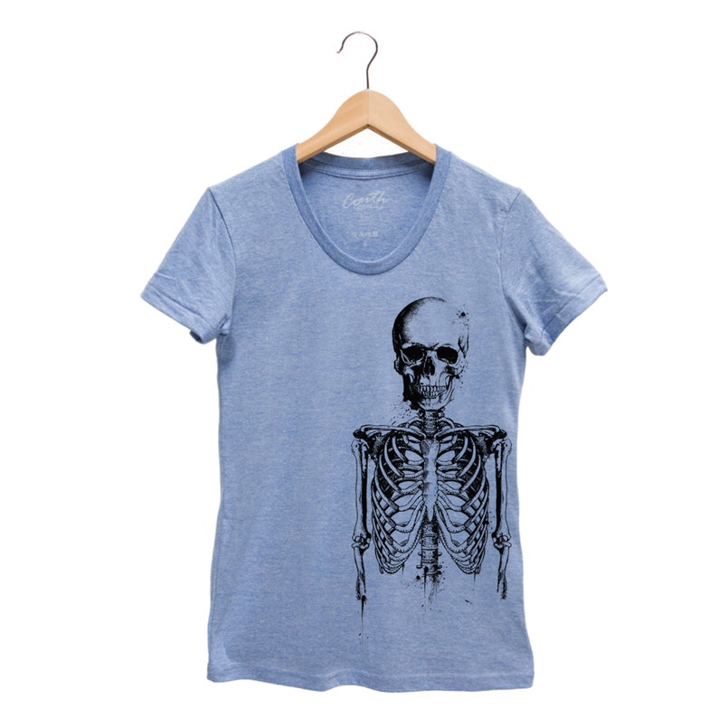 Puede incluir: Una camiseta azul claro con un estampado gr&aacute;fico en blanco y negro de un esqueleto. El esqueleto est&aacute; de pie con los brazos a los lados. El cr&aacute;neo est&aacute; mirando hacia adelante con una expresi&oacute;n neutral.