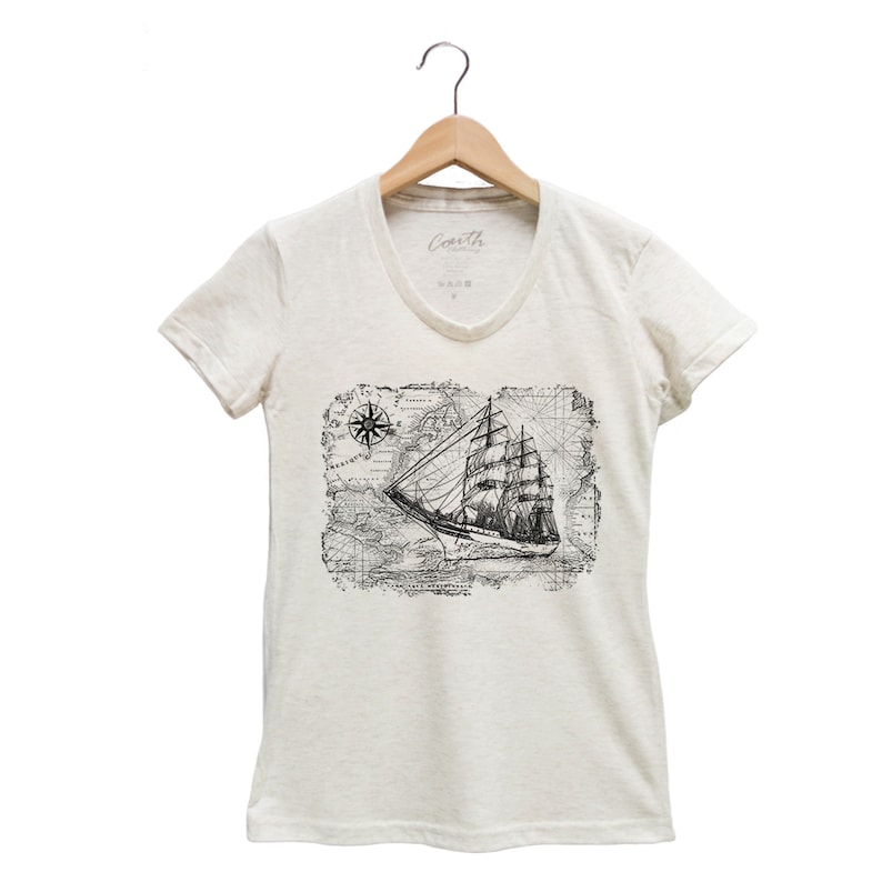 Puede incluir: Una camiseta blanca de cuello en V con un estampado gr&aacute;fico en blanco y negro de un barco navegando en un mapa vintage con una br&uacute;jula.