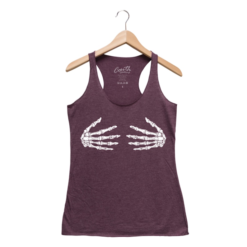 May include: A maroon racerback tank top with a white skeleton hand graphic. The tank top is hanging on a wooden hanger. The brand name "Coarth Clothing" is printed on the top of the tank top.