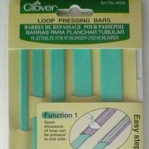 Könnte beinhalten: Ein Satz mit vier grünen Kunststoff-Schleifen-Pressstäben zum Erstellen von 3D-Schleifen mit einem Bügeleisen. Die Stäbe sind mit dem Clover-Logo und dem Text "3-D loops" gekennzeichnet.