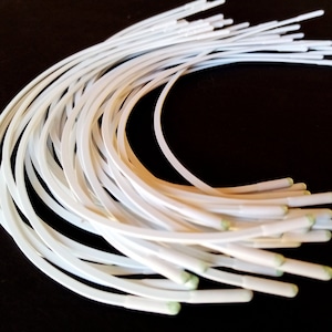 Puede incluir: Un paquete de alambre de diadema de plástico blanco con puntas verdes. El alambre está doblado en forma de semicírculo.