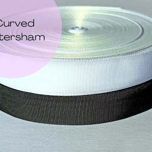 May include: A close-up of two rolls of curved Petersham ribbon. One roll is white, and the other is black. The white ribbon is on top of the black ribbon. The text "Curved Petersham" is in a pink circle in the upper left corner.