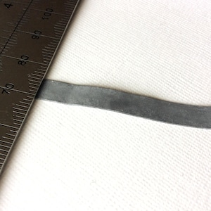Puede incluir: Primer plano de una tira de metal plateada, que mide aproximadamente 17,8 cm de largo, colocada junto a una regla.