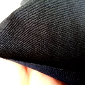 Puede incluir: Primer plano de tela negra con tejido texturizado. La tela tiene un brillo sutil y un borde ligeramente elevado.