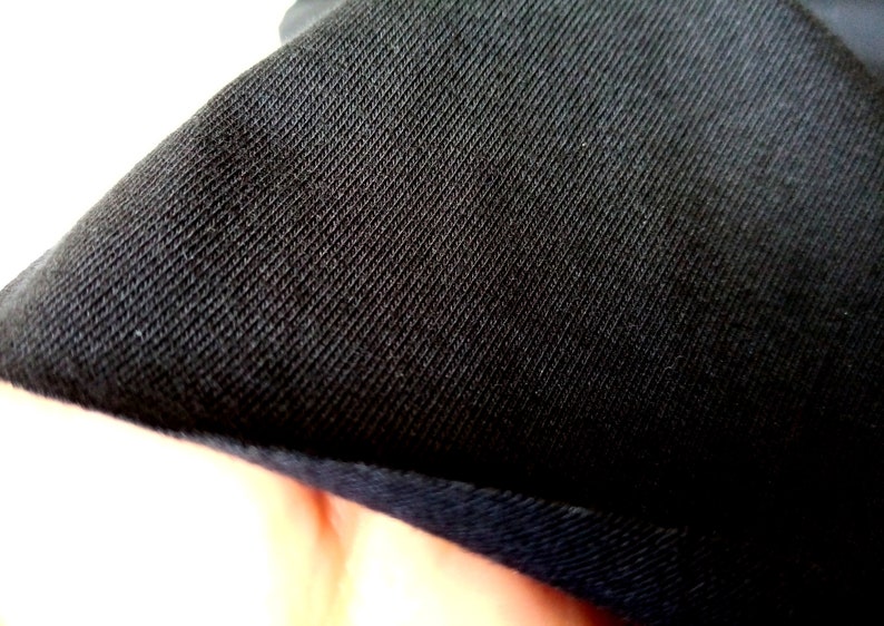 Puede incluir: Primer plano de tela negra con tejido texturizado. La tela tiene un brillo sutil y un borde ligeramente elevado.
