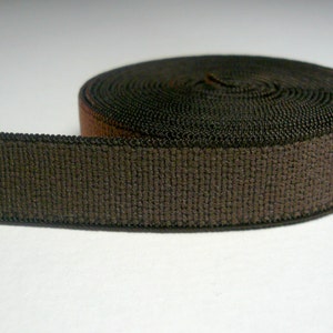 May include: A roll of dark brown elastic band featuring a woven, textured surface. The material is coiled into a circular shape, showing a consistent dark brown color throughout the length of the flat, flexible fabric strip.