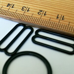 May include: Black metal slider buckles for sewing projects. The buckles are shown next to a ruler, with the largest buckle measuring approximately 1 1/2 inches in length.