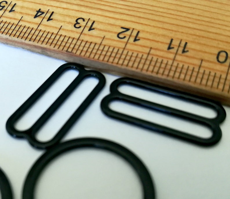 May include: Black metal slider buckles for sewing projects. The buckles are shown next to a ruler, with the largest buckle measuring approximately 1 1/2 inches in length.