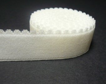 May include: A roll of white hook and loop tape with a decorative edge. The tape is soft and fuzzy.