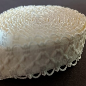 May include: A roll of white, decorative trim with a scalloped edge. The trim is made of a soft, woven fabric and has a delicate, floral pattern.