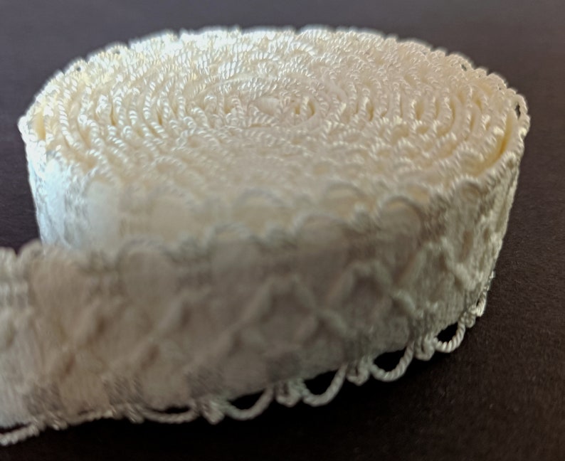 May include: A roll of white, decorative trim with a scalloped edge. The trim is made of a soft, woven fabric and has a delicate, floral pattern.