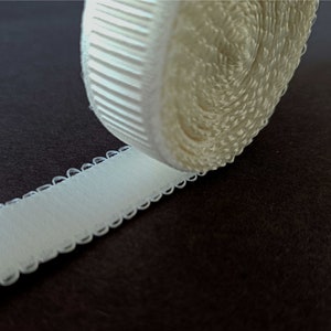 Peut inclure: Un rouleau de bretelle de soutien-gorge &eacute;lastique blanche avec un bord festonn&eacute;. La bretelle est enroul&eacute;e et le bord est visible.