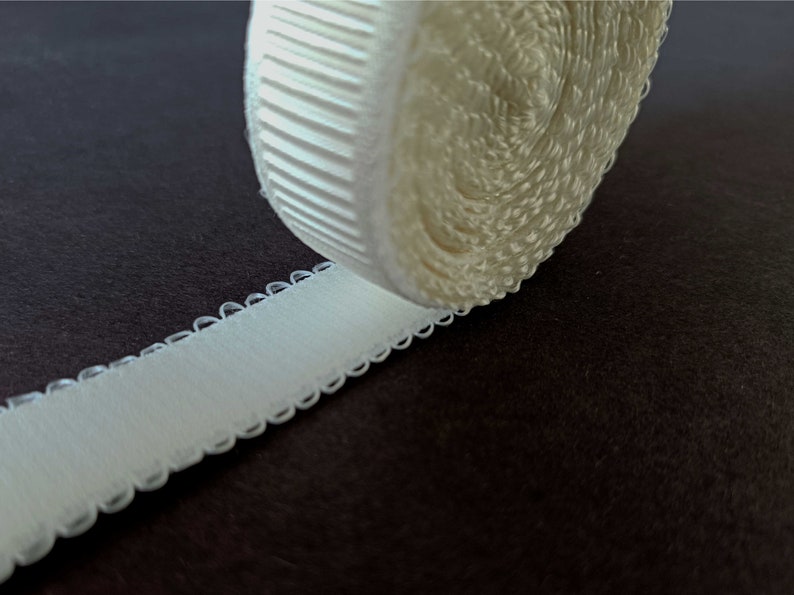 Peut inclure: Un rouleau de bretelle de soutien-gorge &eacute;lastique blanche avec un bord festonn&eacute;. La bretelle est enroul&eacute;e et le bord est visible.