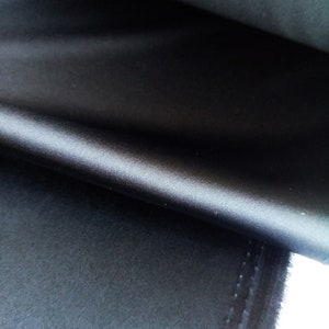 Könnte beinhalten: Nahaufnahme eines schwarzen Satin-Stoffes mit einer glatten, seidenartigen Textur. Der Stoff ist umgeklappt und zeigt die Unterseite.