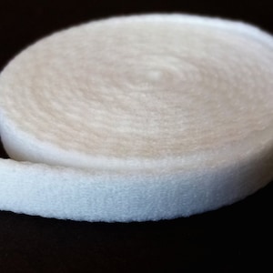 May include: A roll of white, soft, and textured fabric, likely felt or a similar material, is displayed against a dark background. The fabric is rolled up, showing its circular form and the texture of the material.