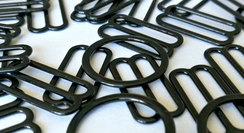 May include: A close-up of a pile of black metal slider buckles. The buckles are in various shapes and sizes, including round and rectangular.