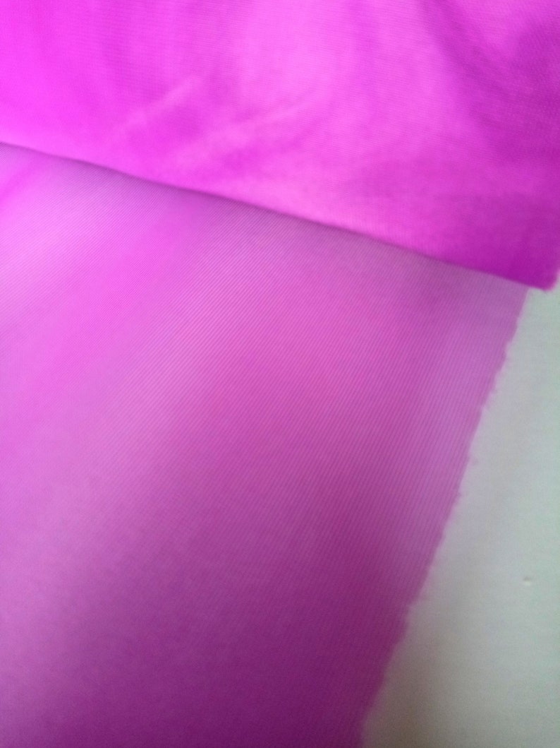 Peut inclure: Gros plan sur un tissu transparent rose vif avec une texture subtile. Le tissu est pli&eacute;, r&eacute;v&eacute;lant une nuance de rose plus claire en dessous.