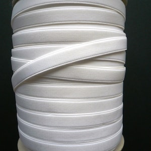 May include: A roll of white elastic trim with a slight sheen. The trim is folded and rolled up on a cardboard core.