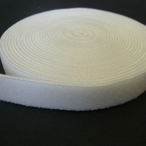 May include: White hook and loop tape, also known as Velcro, rolled up on a black surface.
