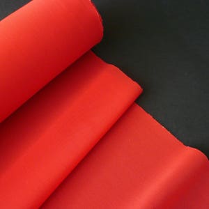 Puede incluir: Un rollo de tela roja brillante, doblado por la mitad, sobre un fondo negro.