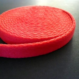 May include: A roll of bright red woven webbing, a type of flat, narrow fabric used for straps, belts, and other applications.
