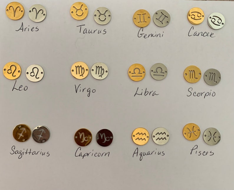 May include: Twelve gold and silver charms featuring the astrological signs of the zodiac. The signs are Aries, Taurus, Gemini, Cancer, Leo, Virgo, Libra, Scorpio, Sagittarius, Capricorn, Aquarius, and Pisces.