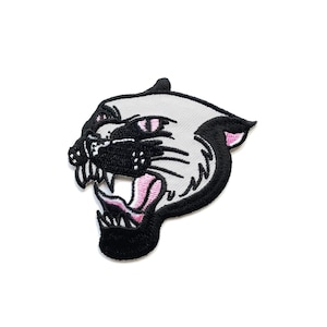 Pode incluir: Um remendo bordado de uma pantera rosnado, com bordado preto e branco e dentes e olhos cor-de-rosa.