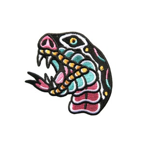 Puede incluir: Un parche bordado colorido de la cabeza de una serpiente con la boca abierta, con detalles en negro, rosa, amarillo y turquesa.