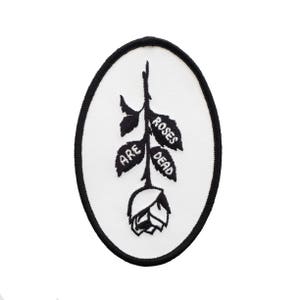 May include: Black and white embroidered patch of a rose with the words "Roses Are Dead" on the petals.