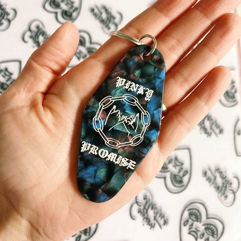 Puede incluir: Un llavero de motel negro y azul con el texto "PINKY PROMISE" y un gr&aacute;fico de dos manos haciendo una promesa me&ntilde;ique.