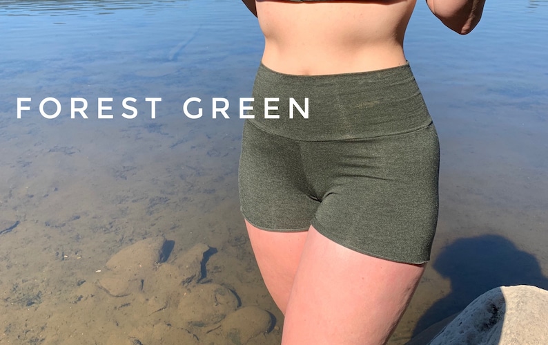 May include: Forest green high-waisted shorts made from a soft, stretchy fabric. The shorts are shown on a person standing in front of a body of water.