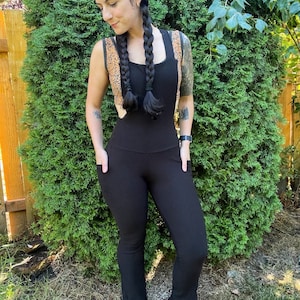 May include: Black jumpsuit with a wide leg and a brown floral pattern on the straps. The jumpsuit has pockets on the front and a fitted waist.