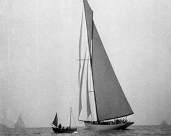 May include: A black and white photograph of two sailboats on the water. The larger sailboat has a large sail and is in the foreground. The smaller sailboat is in the background.