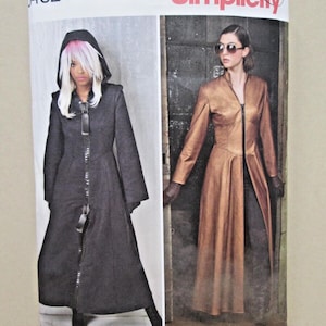 May include: A Simplicity 8482 sewing pattern envelope for a long coat in sizes 14-22. The front shows two variations: a black hooded coat with a front zipper and a metallic bronze coat with a front zipper, both featuring long sleeves.
