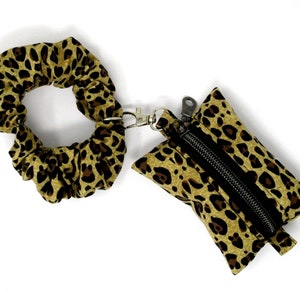 May include: A brown and black leopard print scrunchie attached to a small brown and black leopard print zippered pouch with a silver zipper and a silver key ring.