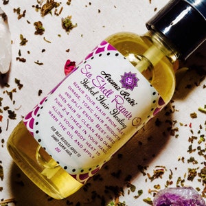 May include: A clear glass bottle with a purple and pink label that reads "Aroma Reiki Sea Shell Repair Oil Herbal Hair Healing". The label also includes the symbol Om. The bottle is sitting on a white surface with green and purple crystals.