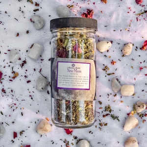 May include: A glass jar filled with a blend of dried herbs and flowers for a New Moon herbal tea. The label reads "Aroma Reiki New Moon Herbal Tea" and includes instructions for setting intentions and creating dreams and goals.