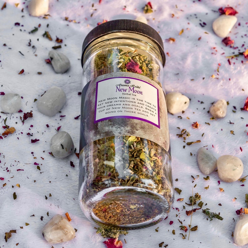 May include: A glass jar filled with a blend of dried herbs and flowers, labeled "New Moon Herbal Tea". The label reads "New Moon Magic is the time to set new intentions and create your dreams and goals. Brew a cup of New Moon Tea and get going on those goals."